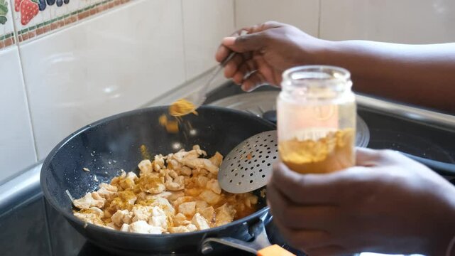 Woman is seasoning chicken breast pieces with curry powder from a jar, during the preparation of a dish
