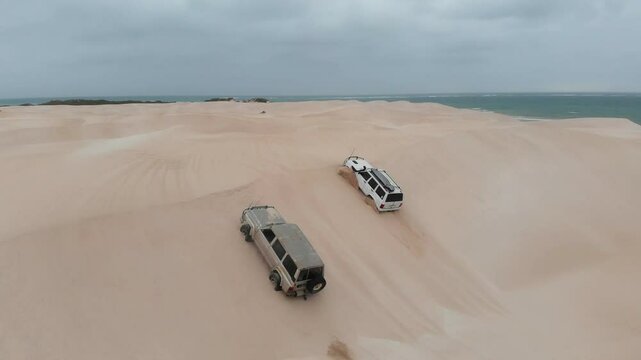 Aerial view of 4x4 vehicles driving on scenic sand dunes in a rugged desert landscape, Geraldton, Australia.
