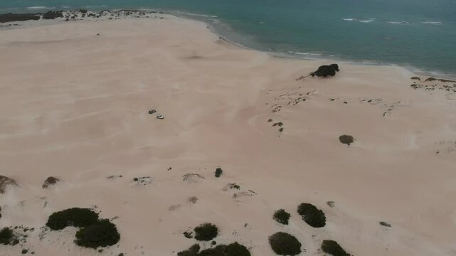 Aerial view of sandy dunes with a 4x4 vehicle driving along the coastline, Geraldton, Australia.