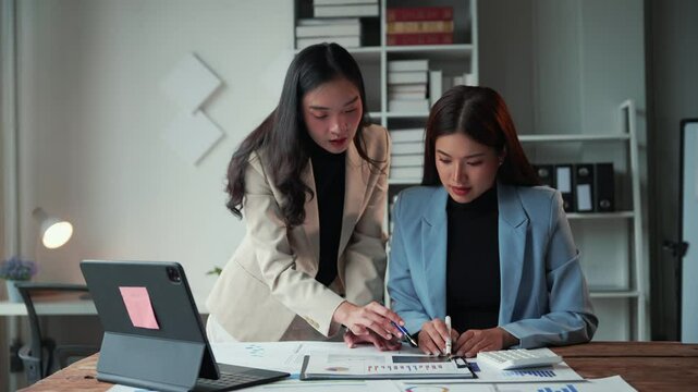 Businesswomen collaboratively reviewing financial data and charts. Focused and engaged in team discussion with digital device at hand