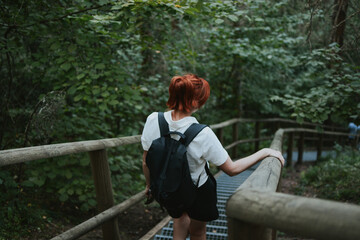 Fototapeta premium female hiker with a backpack goes down the stairs with railings in the depths of the forest