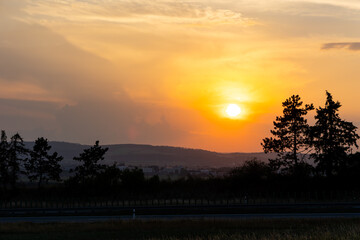 Orange sunset sun getting down amongs the trees over the road in the shade. Dramatic orange sky during the susnset.