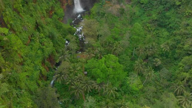 Aerial view of kapas biru waterfall cascading through lush jungle and serene river, lumajang, indonesia.