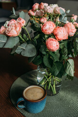 A bouquet of pink and white roses on a wooden table in the living room. A bouquet and a cup of coffee for the woman you love