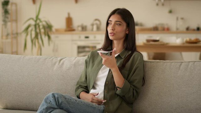 Muslim woman Arabian girl Islamic lady female talking mobile phone loudspeaker dictate talk speech speak to smartphone microphone call record audio message recording voice mail at home couch kitchen
