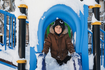 happy child boy is playing on a playground on a slide outside in winter.