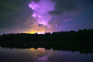 Obraz premium lightning strikes at night behind the clouds in the reflection of the lake in autumn