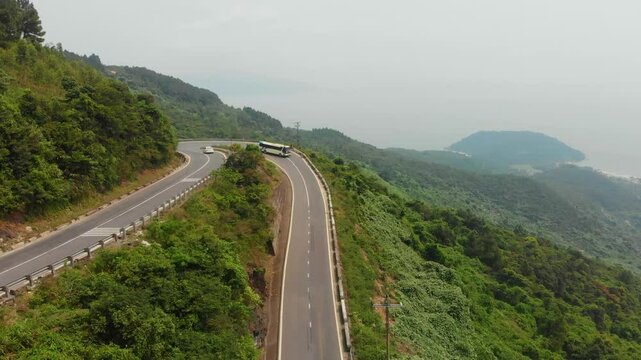 Aerial view of winding road through lush mountains with traffic including motorcycles and trucks, Hai Van Pass, Vietnam.