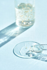 Luxurious skincare serum with gold flakes and glass dropper on light blue background in natural sunlight