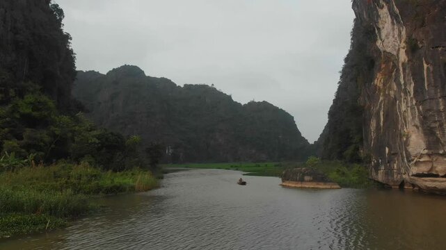 Aerial view of tranquil tam coc landscape with lush green mountains and a winding river filled with boats and people, Ninh Binh, Vietnam.