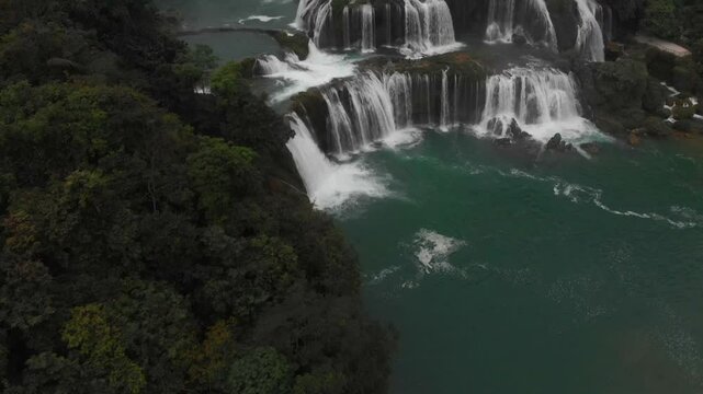 Aerial view of the breathtaking Ban Gioc waterfall cascading into the Quay Son river surrounded by lush forest, Cao Bang, Vietnam.