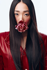 Attractive woman with long black hair in red jacket posing with flower in mouth against white...