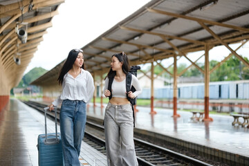 Two women are walking on a train platform with their luggage