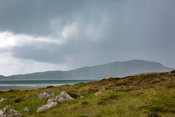 View of Eriskay from South Uist across the water, Image shows the scenic mountain of Eriskay as heavy rainfall pours down  