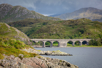 Loch nan Uamh viaduct from across the Loch, Image shows the viaduct located in Loch Nan Uamh on a summers day with clouds surrounding the mountains in the background
