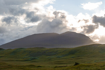 Obraz premium Scottish highlands at sunset, Image shows a mountain range near Glencoe as the sun sets while shining through clouds