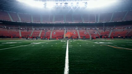 Wide-angle view of an empty football stadium, with camera zooming out to reveal rows of red seats under intense stadium lights