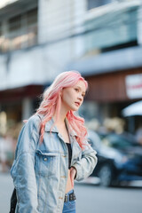 A woman with pink hair stands on a city street