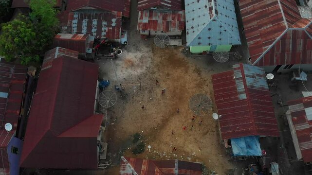 Aerial view of children playing soccer in a rustic village at sunset with fishing homes and trees, Tanjung Binga, Indonesia.