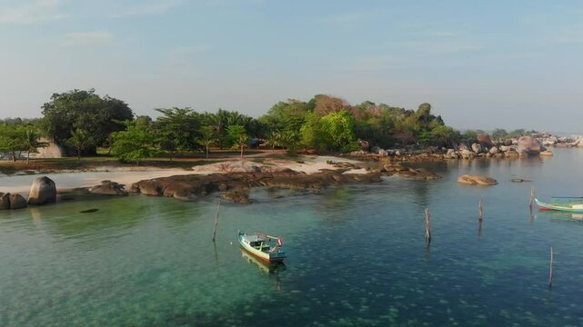 Aerial view of serene beach with granite boulders and a boat at sunrise, Tanjung Tinggi, Indonesia.