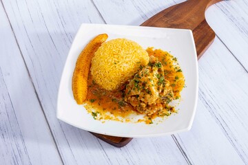 A vibrant, traditional Ecuadorian dish, Seco de Pollo, served with flavorful yellow rice and fried plantains. The dish features a tender chicken leg simmered in a rich, aromatic sauce made from tomato