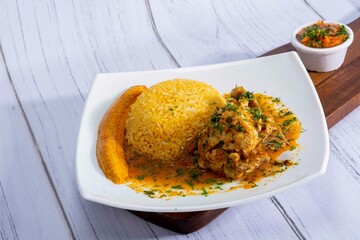 A vibrant, traditional Ecuadorian dish, Seco de Pollo, served with flavorful yellow rice and fried plantains. The dish features a tender chicken leg simmered in a rich, aromatic sauce made from tomato