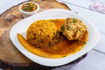 A vibrant, traditional Ecuadorian dish, Seco de Pollo, served with flavorful yellow rice and fried plantains. The dish features a tender chicken leg simmered in a rich, aromatic sauce made from tomato