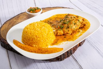 A vibrant, traditional Ecuadorian dish, Seco de Pollo, served with flavorful yellow rice and fried plantains. The dish features a tender chicken leg simmered in a rich, aromatic sauce made from tomato