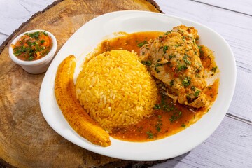 A vibrant, traditional Ecuadorian dish, Seco de Pollo, served with flavorful yellow rice and fried plantains. The dish features a tender chicken leg simmered in a rich, aromatic sauce made from tomato