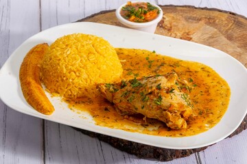A vibrant, traditional Ecuadorian dish, Seco de Pollo, served with flavorful yellow rice and fried plantains. The dish features a tender chicken leg simmered in a rich, aromatic sauce made from tomato