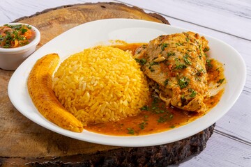 A vibrant, traditional Ecuadorian dish, Seco de Pollo, served with flavorful yellow rice and fried plantains. The dish features a tender chicken leg simmered in a rich, aromatic sauce made from tomato