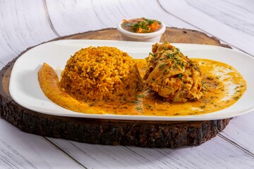 A vibrant, traditional Ecuadorian dish, Seco de Pollo, served with flavorful yellow rice and fried plantains. The dish features a tender chicken leg simmered in a rich, aromatic sauce made from tomato