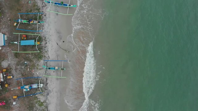 Aerial view of traditional fishing boats on a beautiful beach with waves, Manggar, Indonesia.