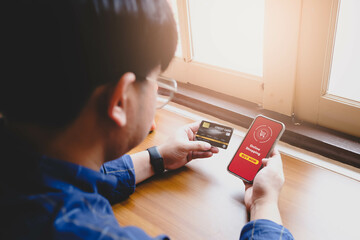 A man holds a credit card and uses a smartphone for online shopping, with a "Buy Now" button visible, highlighting digital payment and e-commerce convenience.