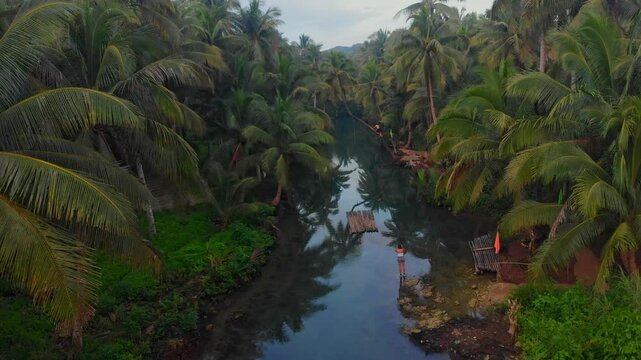 Aerial view of a serene river surrounded by lush palm trees and a tranquil forest at sunrise, Maasin, Philippines.