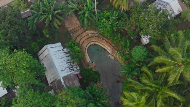 Aerial view of a serene village by a river surrounded by lush palm trees and forest at sunrise, Maasin, Philippines.