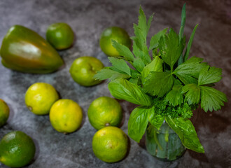 mehrere gelbe und grüne Limetten, Paprika und ein Kräuterglas Liebstöckel, Lauch, Basilikum, mit grauer Hintergrund, 
