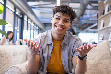 On video call, Smiling man sitting on sofa in modern office, gesturing with hands