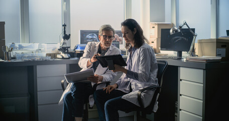 Male and female scientists in lab coats conduct scientific research, look at papers and use tablet...