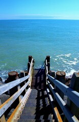 A wooden staircase leads down to a tranquil blue sea under a clear sky, offering serene and...