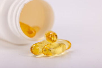 White plastic bottle spilling yellow medicinal capsules on a white surface