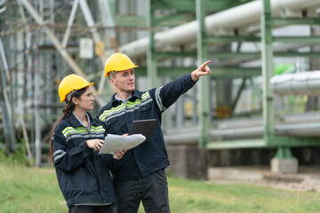 Male and female petrochemical engineers with tablet working at petroleum refinery. Workers survey pipelines for oil and gas in power plant energy industry manufacturing.