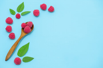 Wooden spoon of ripe raspberries on table, angle view. Three raspberries in one spoon and leaves on a blue wooden table