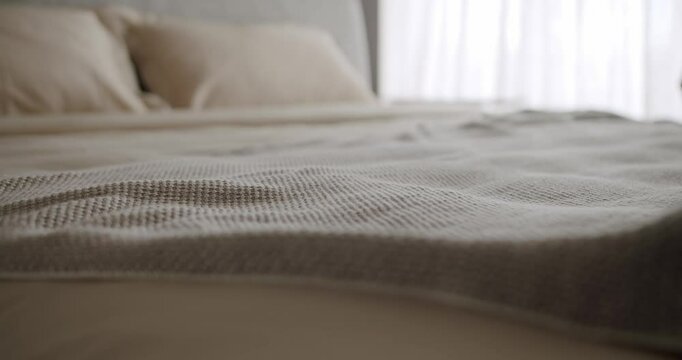 Close-up of a cozy bed featuring a textured blanket and neutral tone bedding, bathed in natural sunlight through sheer curtains, creating a serene and inviting atmosphere. Cozy Bed with Soft Blanket