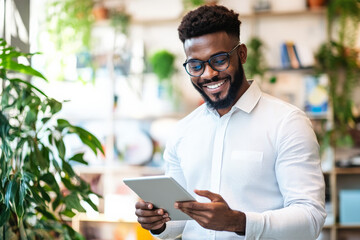 Young Brazilian businessman happily working on his tablet in a contemporary, creatively designed office.