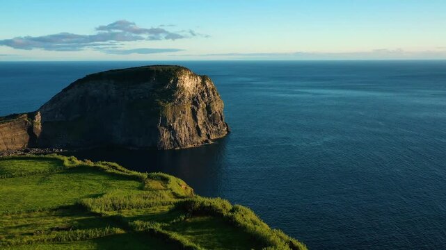 Aerial view of rugged cliffs and serene ocean with lush green grass, Faial, Azores, Portugal.