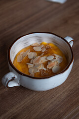 Close-up view of sweat creamy pumpkin crème brûlée dessert (also known as burnt cream or Trinity cream) with almond slices standing on wooden table in restaurant. Soft focus. Desserts theme.