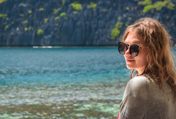 A woman enjoys the serene beauty of a tropical beach, glancing back at the sparkling water and lush cliffs on a sunny day