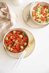 Healthy vegetarian salad with fresh cherry tomato, cucumber, sweet pepper, green olives and lettuce in bowl on white table. Top view