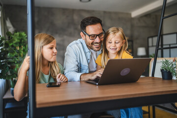 Father and daughters smile and use laptop at home together happy